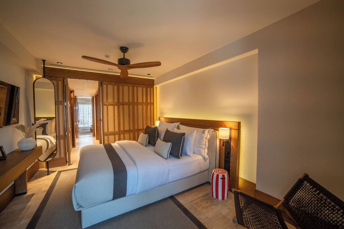Quarto de hotel moderno com uma cama grande, um ventilador de teto, uma mesa de cabeceira e um criado-mudo.