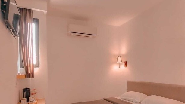 Una habitación de hotel moderna con una cama, una mesita de noche con lámpara, un equipo de aire acondicionado y un televisor fijado a la pared.