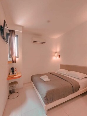 Una habitación de hotel moderna con una cama, una mesita de noche con lámpara, un equipo de aire acondicionado y un televisor fijado a la pared.
