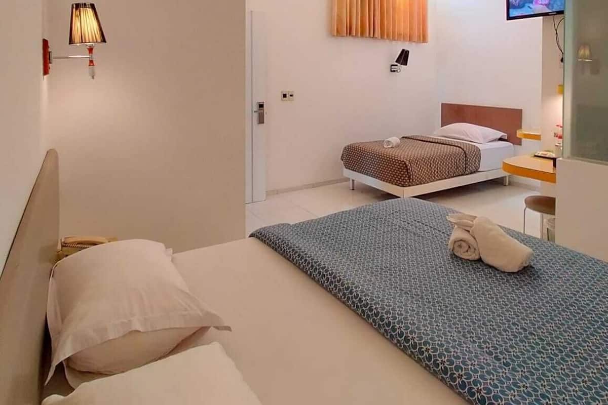 A hotel room with two beds, a desk, a TV, and a window with curtains.