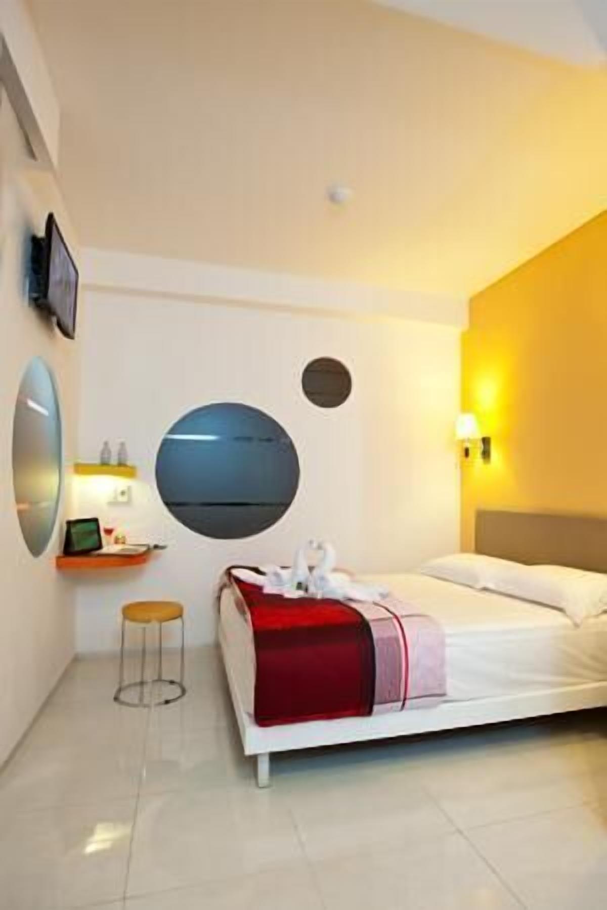 Una habitación de hotel moderna con cama, mesita de noche y televisor montado en la pared.