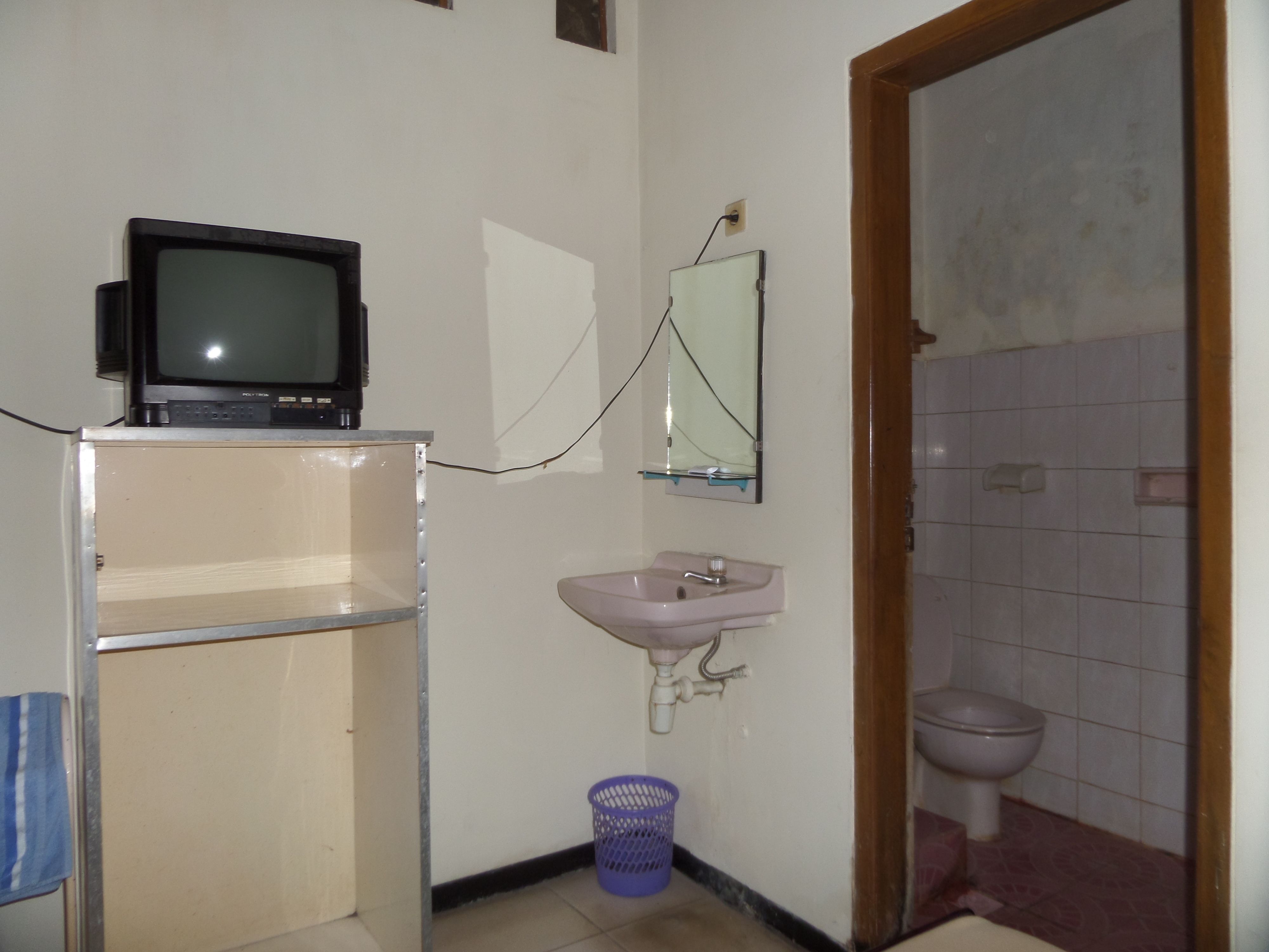 Un baño pequeño con televisión en un estante, lavamanos, espejo e inodoro.