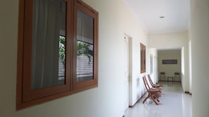 A hallway with wooden-framed windows, a tiled floor, and a view of a balcony with a tiled roof. - Hotel Armi (Malang)