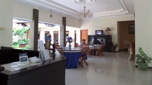 A hotel lobby with a reception desk, a dining area with a chandelier, and a television. - Hotel Armi (Malang)