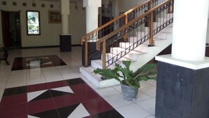 A spacious lobby with a geometric patterned floor, a staircase with a wooden handrail, and a potted plant. - Hotel Armi (Malang)