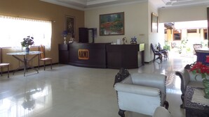 A reception area with a reception desk, chairs, a table with a vase, and a painting on the wall. - Hotel Armi (Malang)