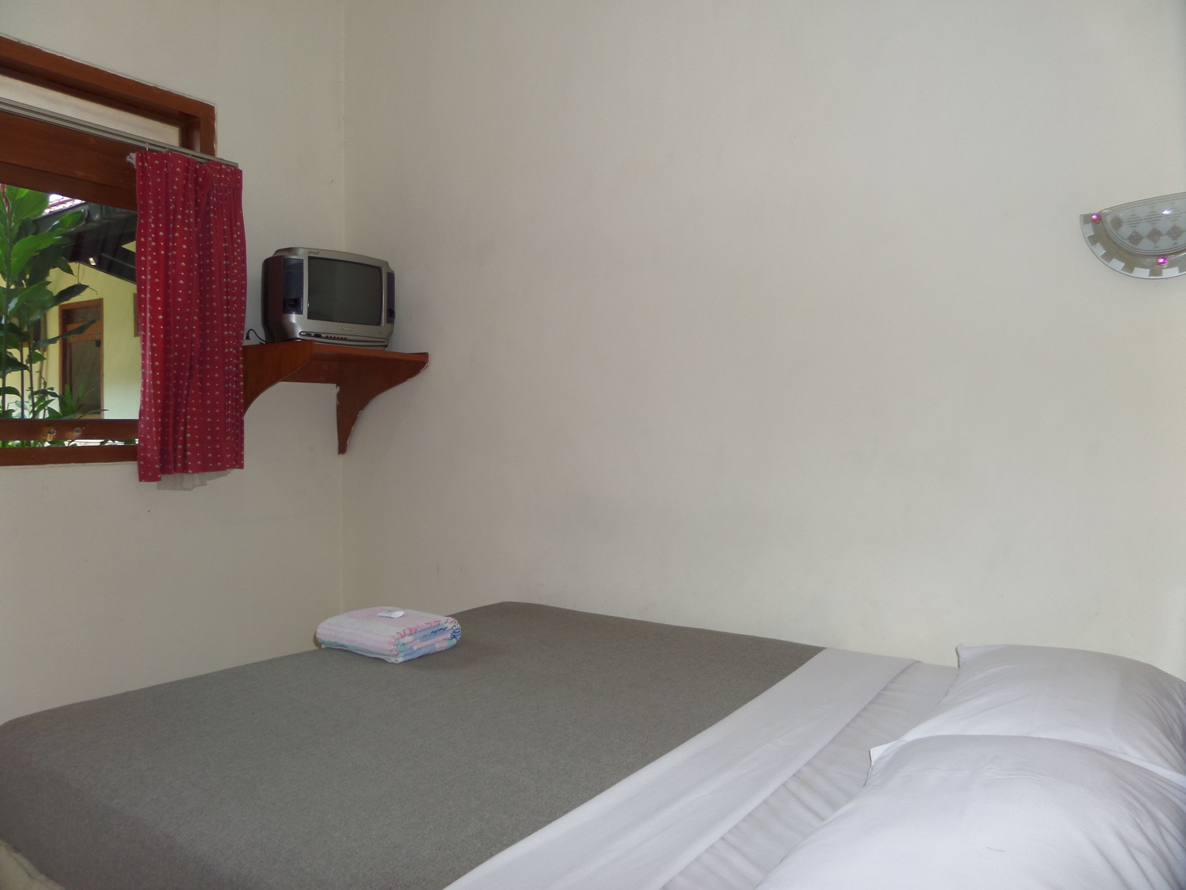 Een kleine kamer met een bed, een televisie op een houten plank en een spiegel aan de muur.