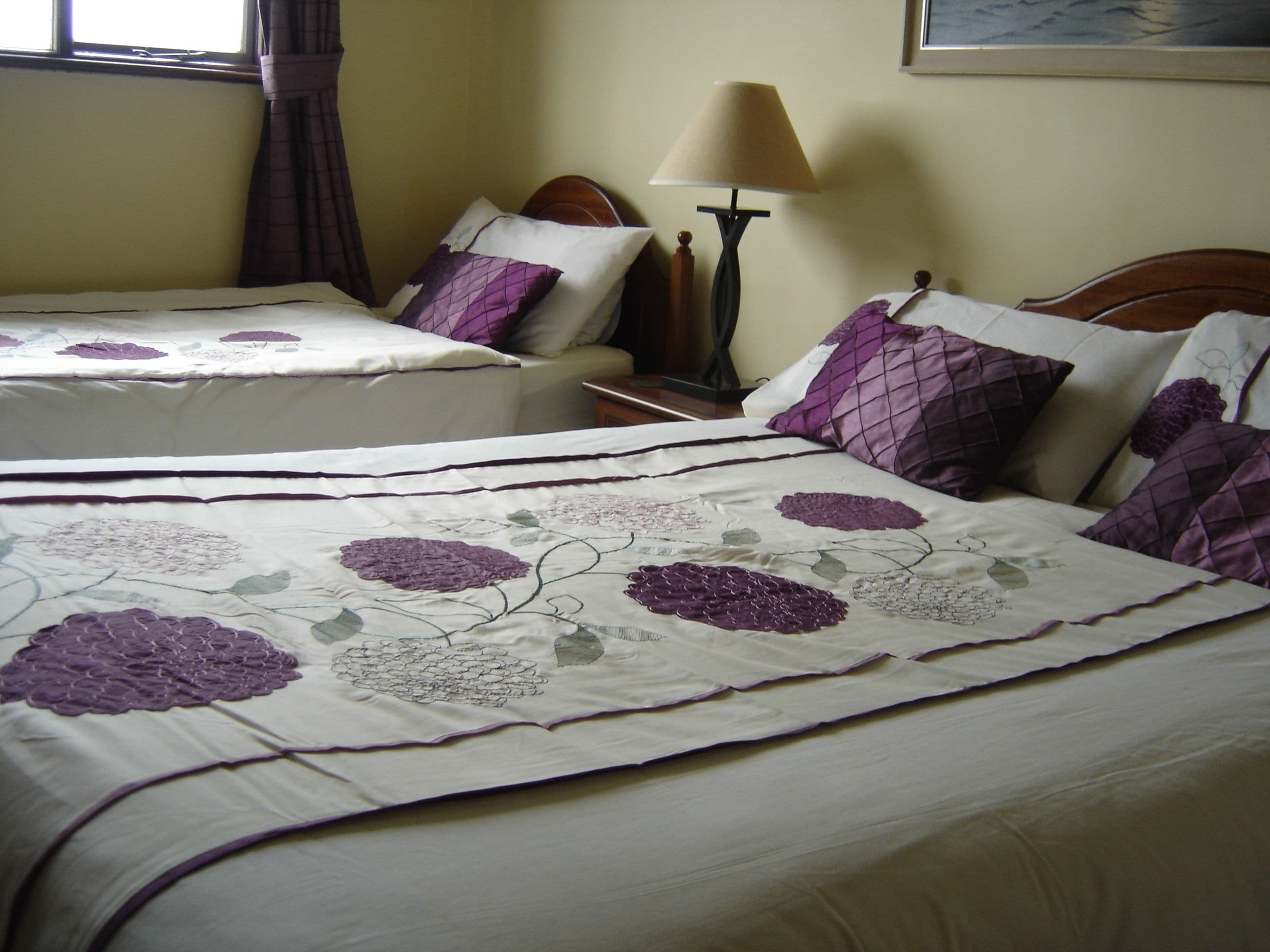 A hotel room with two beds, each with purple floral bedding and matching pillows.