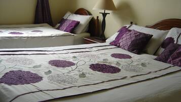 A hotel room with two beds, each with purple floral bedding and matching pillows.