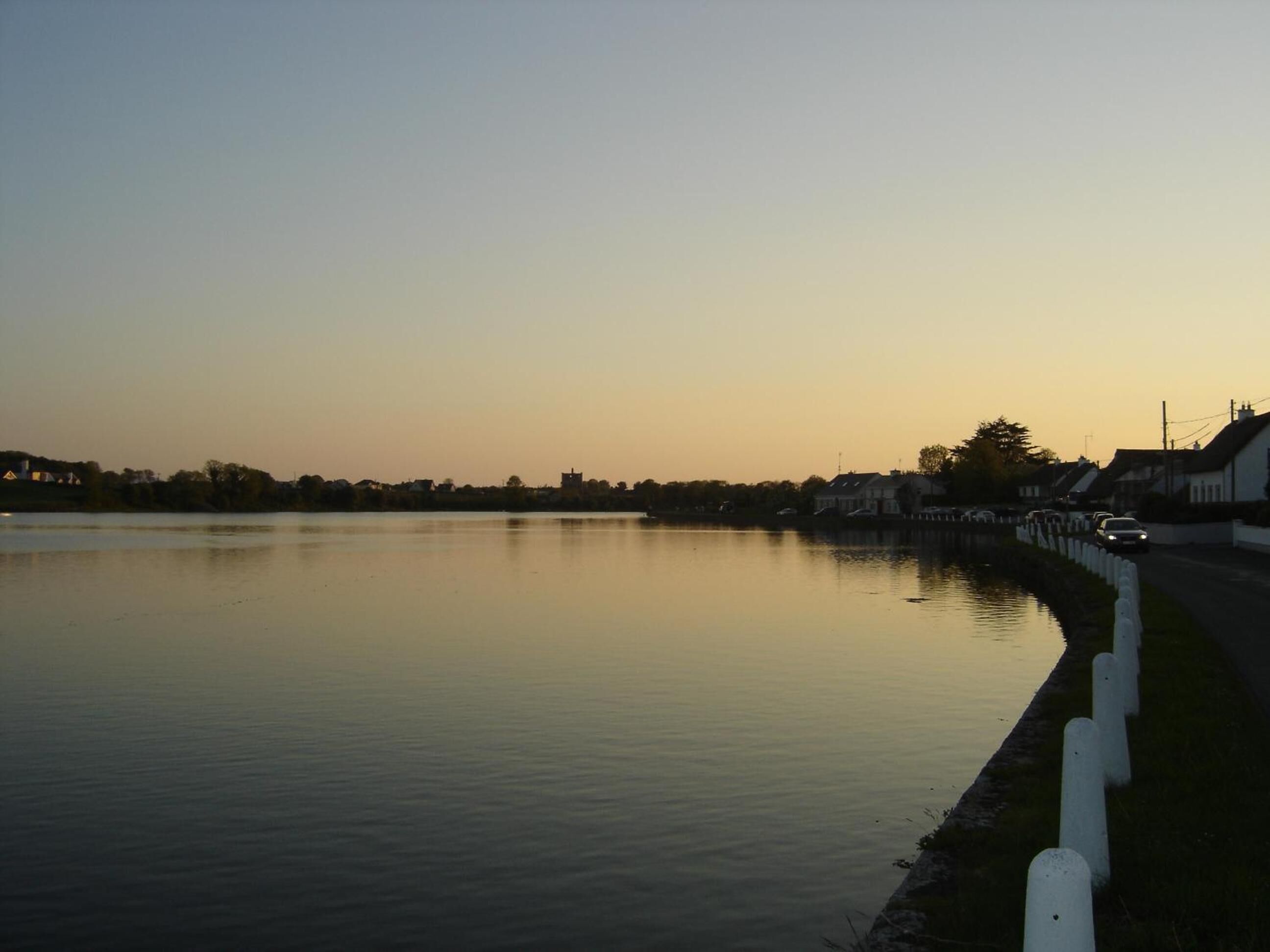 A calm lake with a road and buildings along the shore.