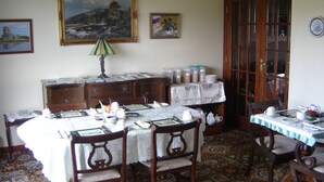 Un coin repas avec une table dressée pour quatre personnes, entourée de chaises en bois. On y trouve un buffet avec des bocaux et une lampe sur la table.