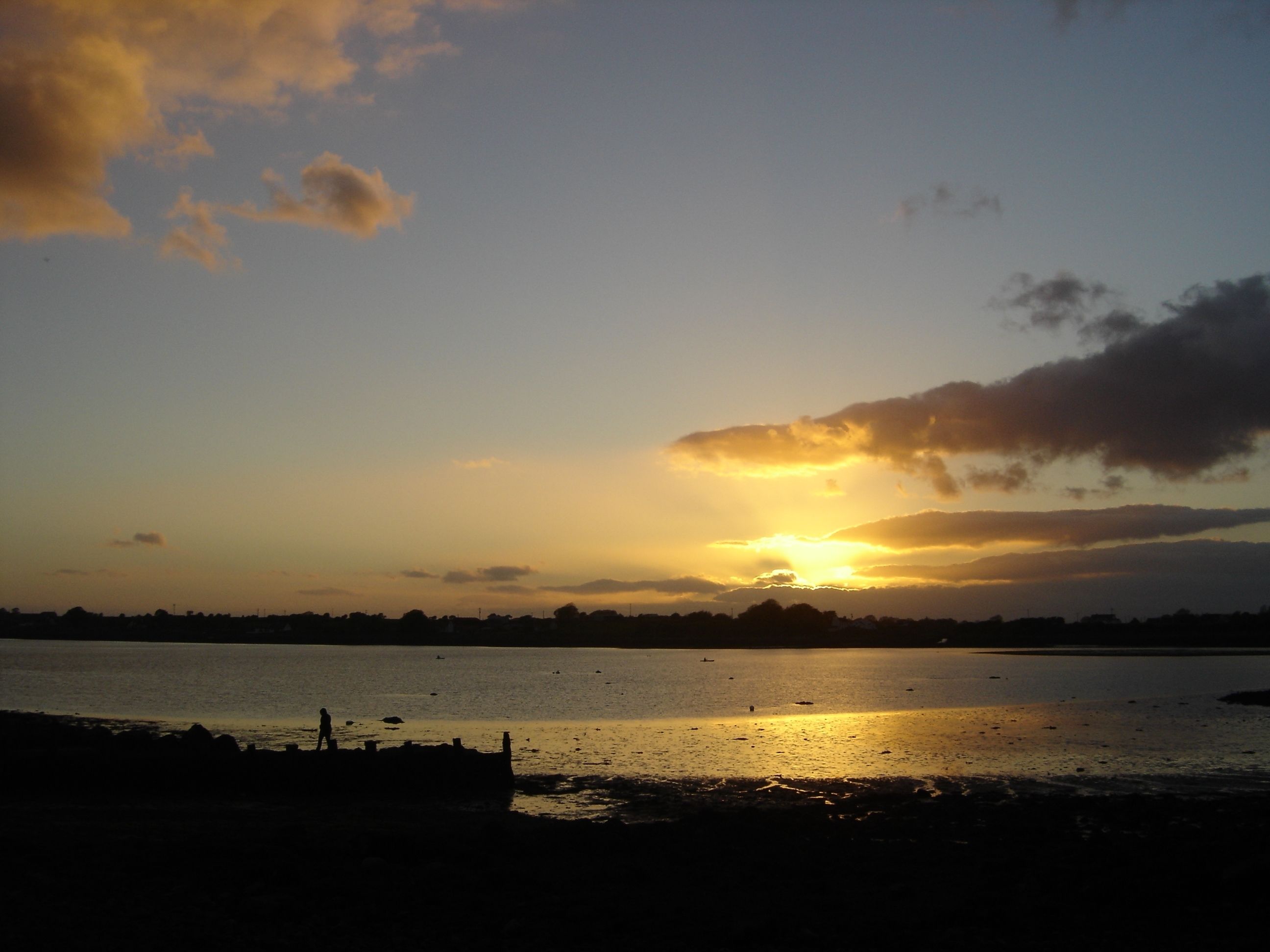 Atardecer sobre una masa de agua tranquila, con la silueta de una costa rocosa y algunas embarcaciones.