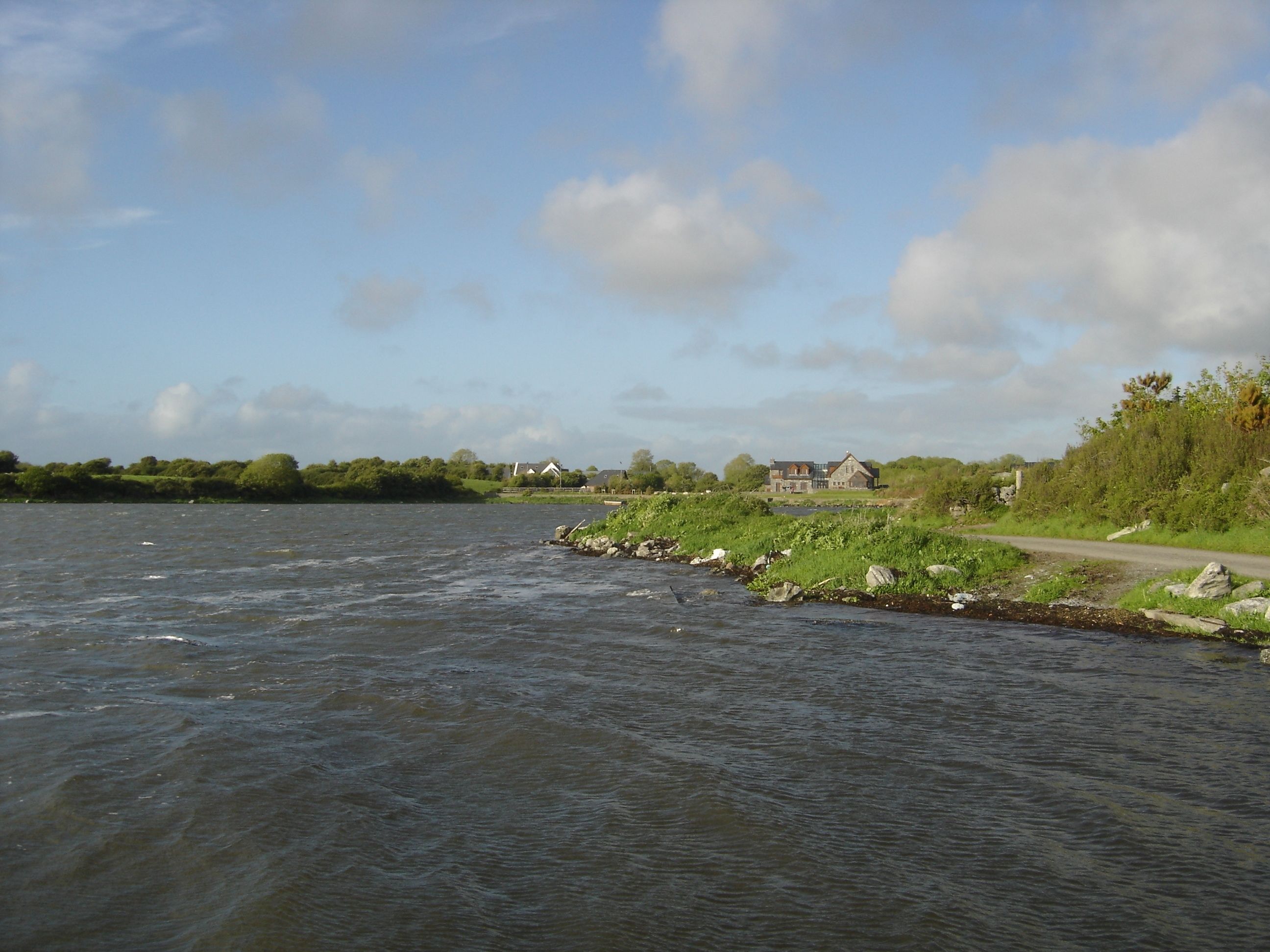 A river with a house on the bank, surrounded by greenery and a clear sky.