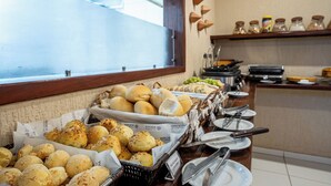 A buffet with various baked goods and a window with blinds. - Pousada Da Germana (Fernando de Noronha)