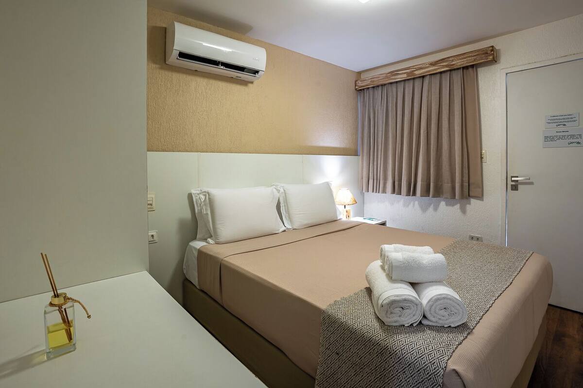 Ein Hotelzimmer mit einem Bett, einem Nachttisch mit Lampe, einer Klimaanlage und einer Tür mit einem Schild.