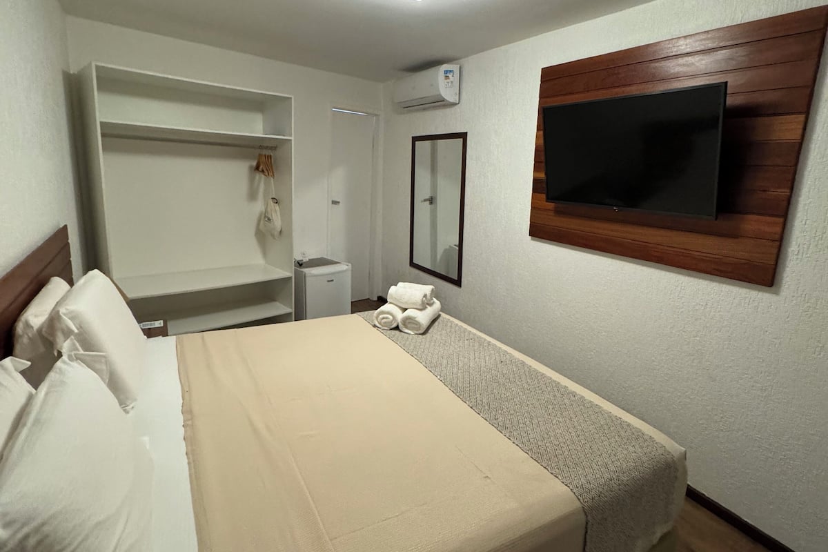 Ein Schlafzimmer mit einem Bett, einem an der Wand befestigten Fernseher, einem Kleiderschrank und einer Klimaanlage.