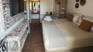 A hotel room with a large bed, a TV mounted on a rustic wall, a small table with toiletries, and a walk-in closet. - Pousada Da Germana (Fernando de Noronha)