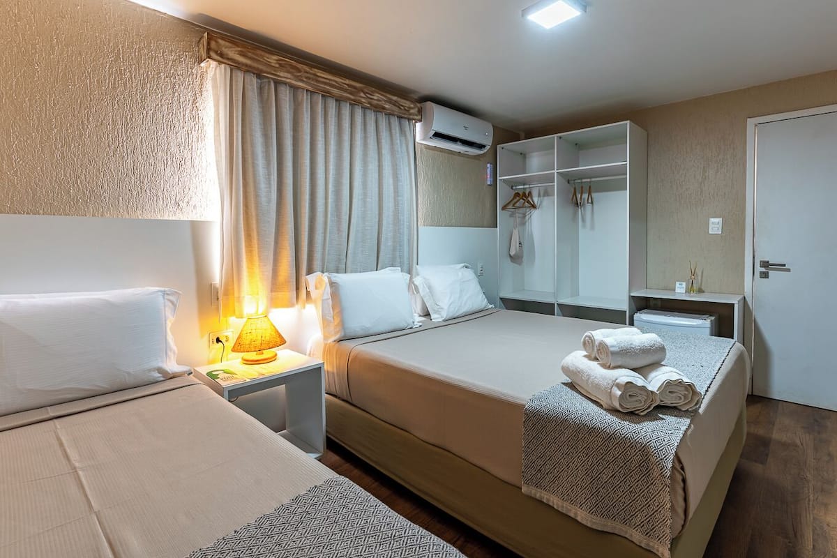 Ein Hotelzimmer mit Bett, Nachttisch, Lampe, Kleiderschrank und Klimaanlage.