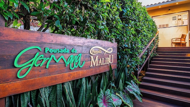 A wooden sign with 'Pousada da Gerimala Malibu' written on it, surrounded by lush green foliage. - Pousada Da Germana (Fernando de Noronha)