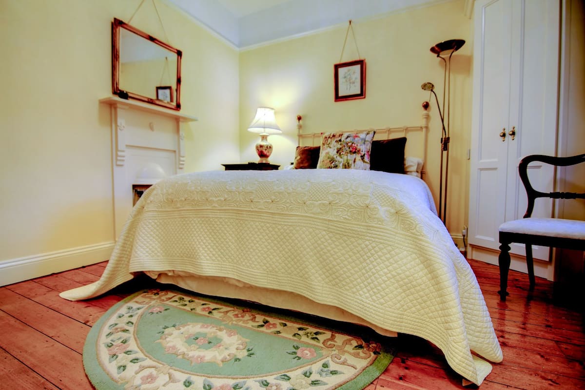 A bedroom with a bed, a chair, a lamp, and a mirror on the wall.
