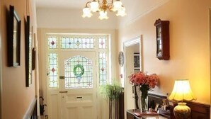 En hall med ett mönstrat golv, en kristallkrona, en vit dörr med målat glas och ett bord med en lampa och blommor.