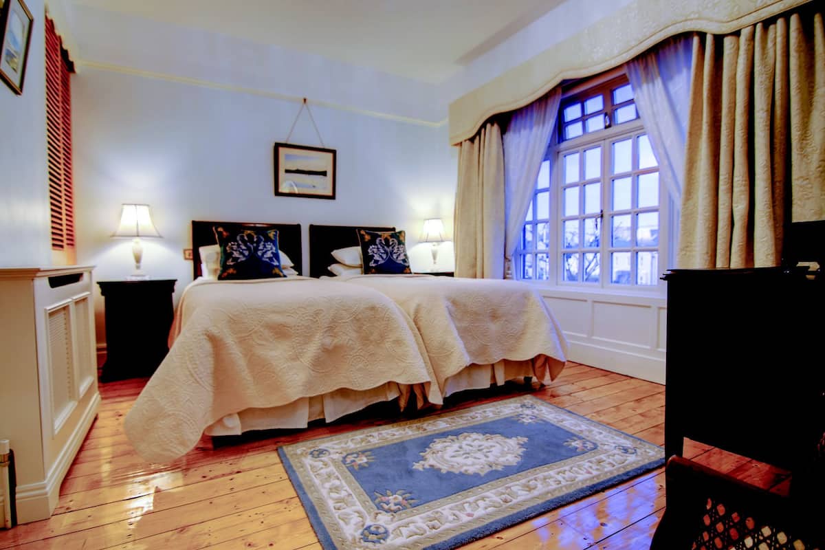 A bedroom with a double bed, two nightstands, a dresser, a window with curtains, and a blue patterned rug.