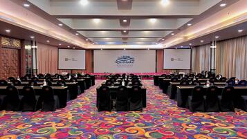 A conference room with a stage, rows of tables, and a colorful carpet.
