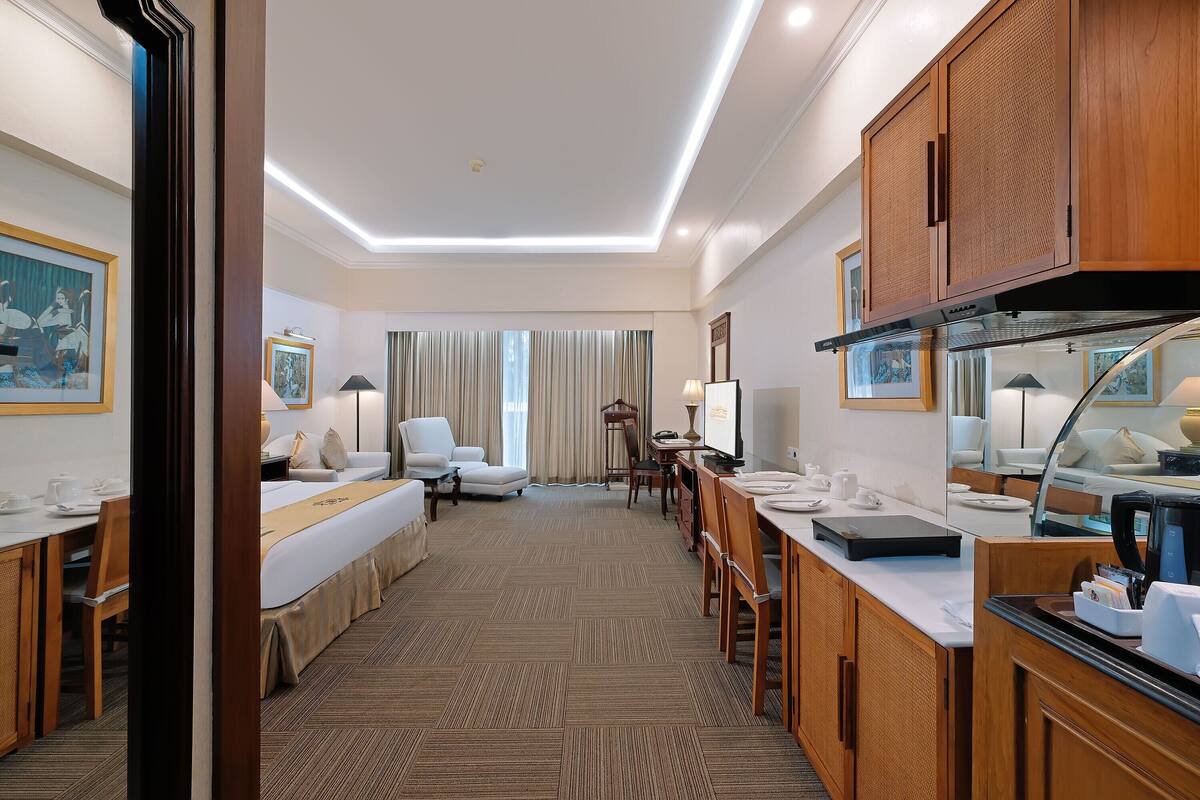 A hotel room with a bed, a desk, a dining area, and a kitchen.