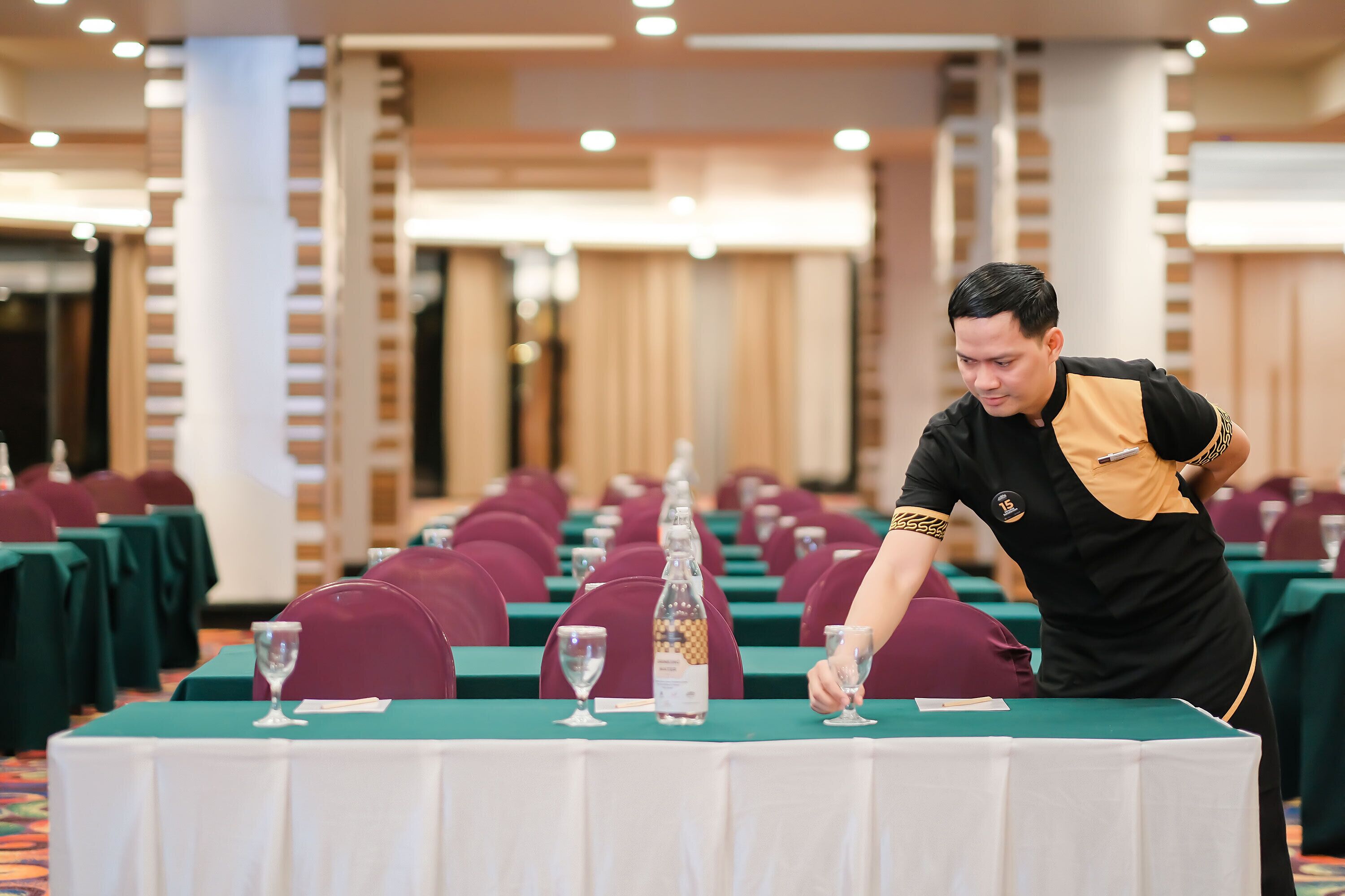 A conference room with rows of tables, each with a glass of water and a bottle of water.