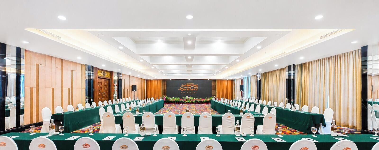 A conference room with long tables, white chairs, and a stage with a banner.