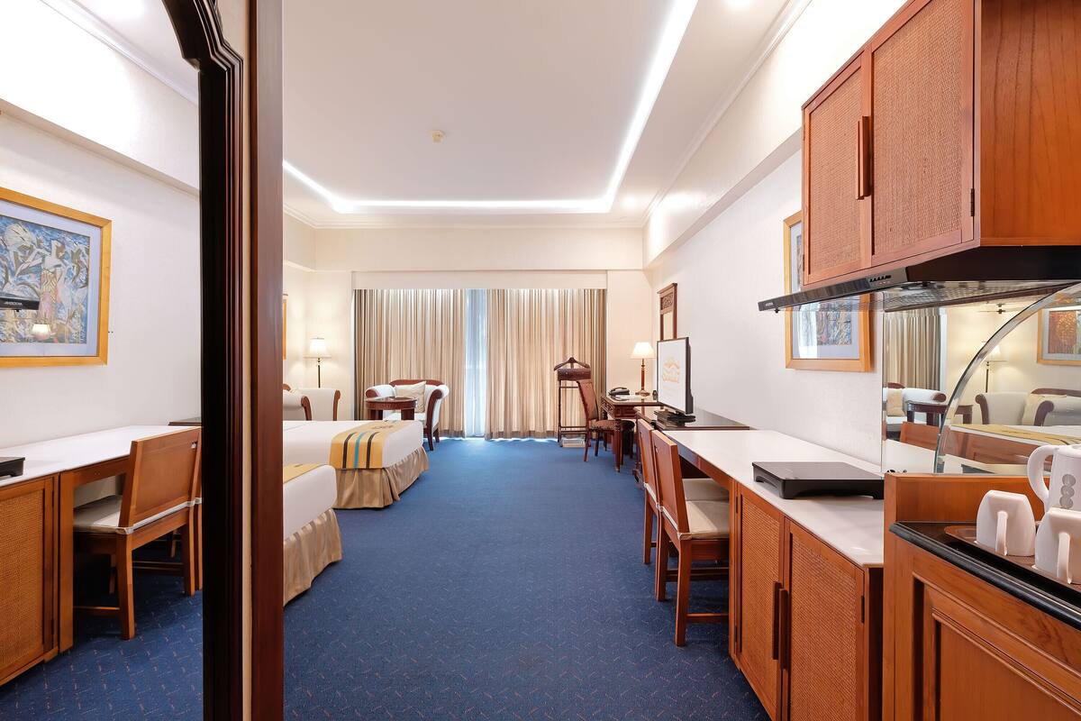 A hotel room with a bed, desk, chairs, and a kitchenette.