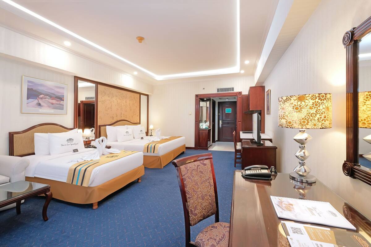 A hotel room with two beds, a desk, a chair, a lamp, and a mirror.