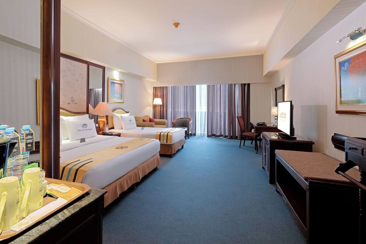 A hotel room with two beds, a desk, a television, and a dining area with a tray of breakfast items.