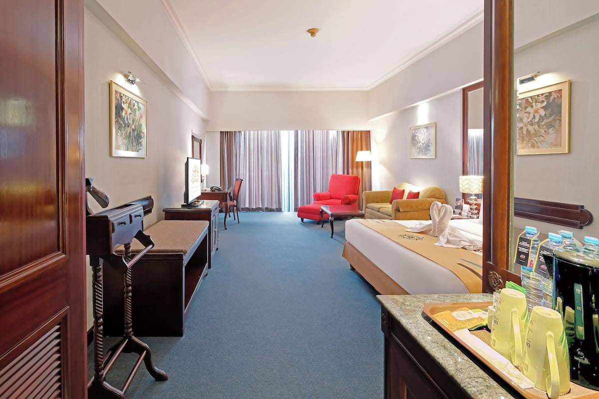 A hotel room with a bed, a desk, a chair, a red armchair, and a coffee station.