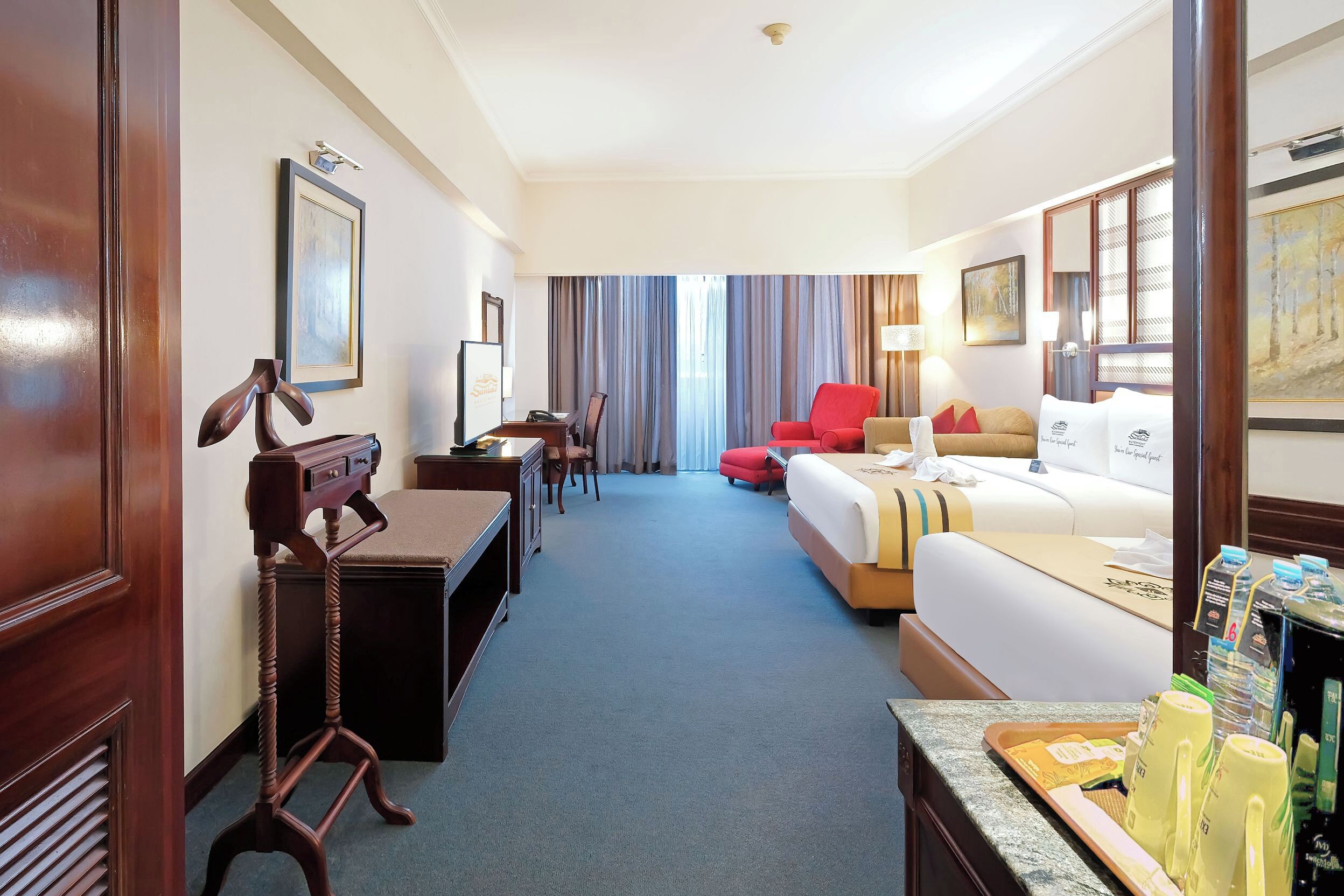 A hotel room with a desk, a bed, a red chair, and a coffee station.