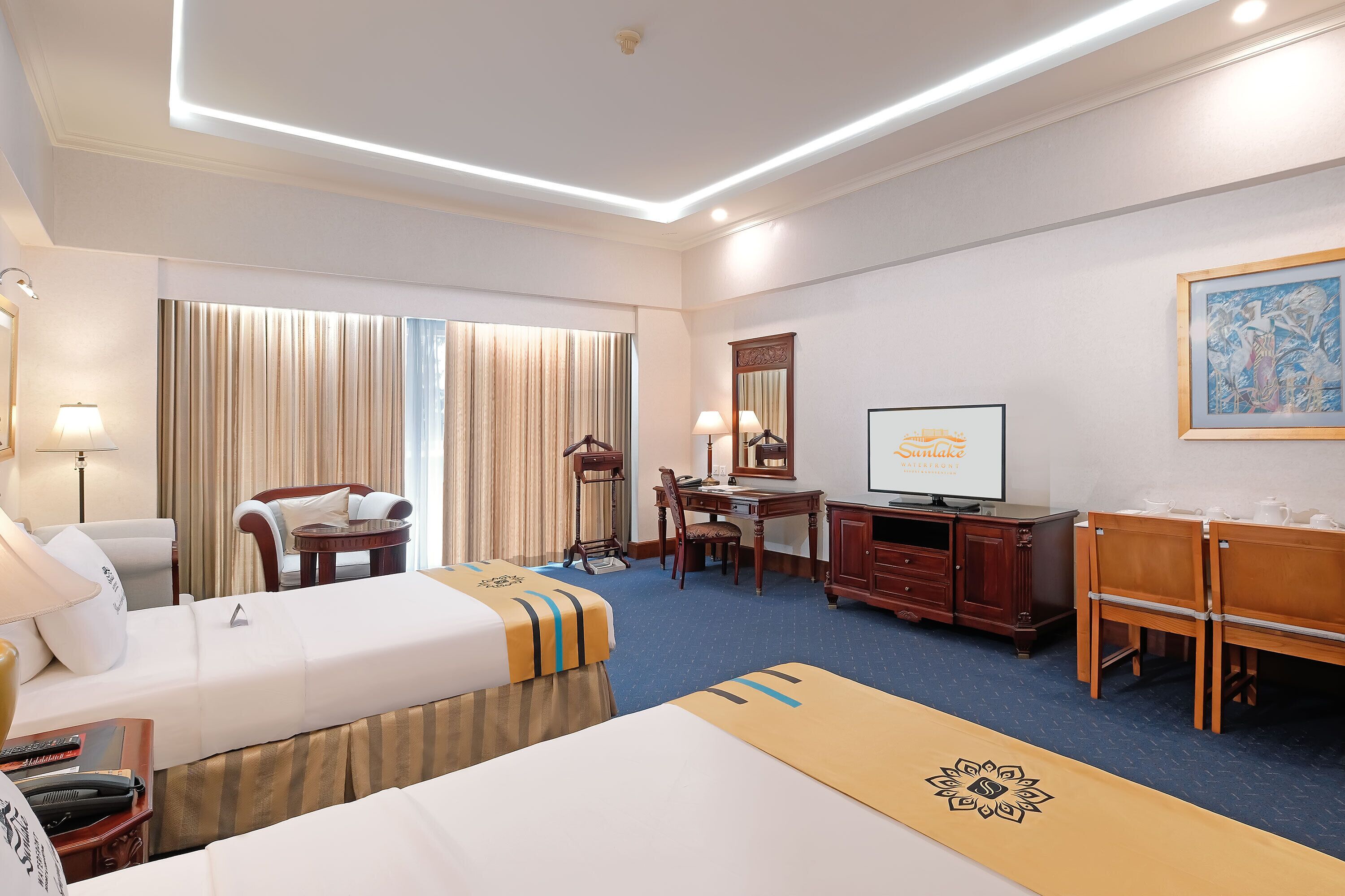 A hotel room with two beds, a desk, a chair, a TV, and a large window with curtains.