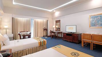 A hotel room with two beds, a desk, a chair, a TV, and a large window with curtains.