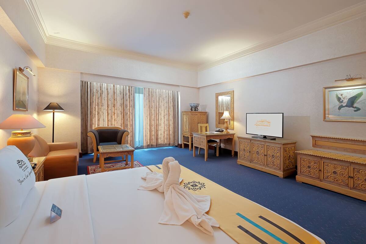 A hotel room with a bed, a desk, a chair, a television, and a wardrobe.