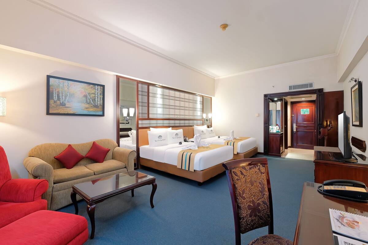 A hotel room with a sofa, a bed with white bedding, a desk with a telephone, and a television.