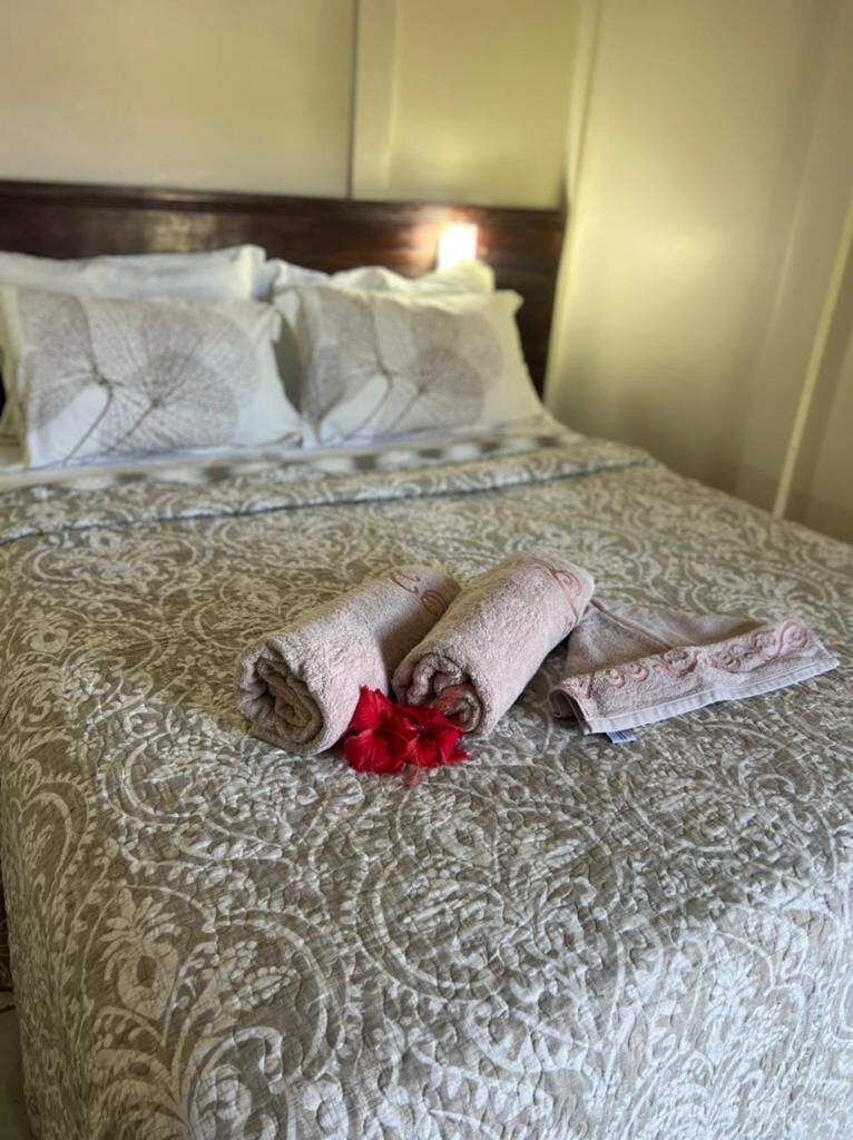 Una cama bien tendida con toallas enrolladas y una flor roja, un edredón estampado y un cabecero.