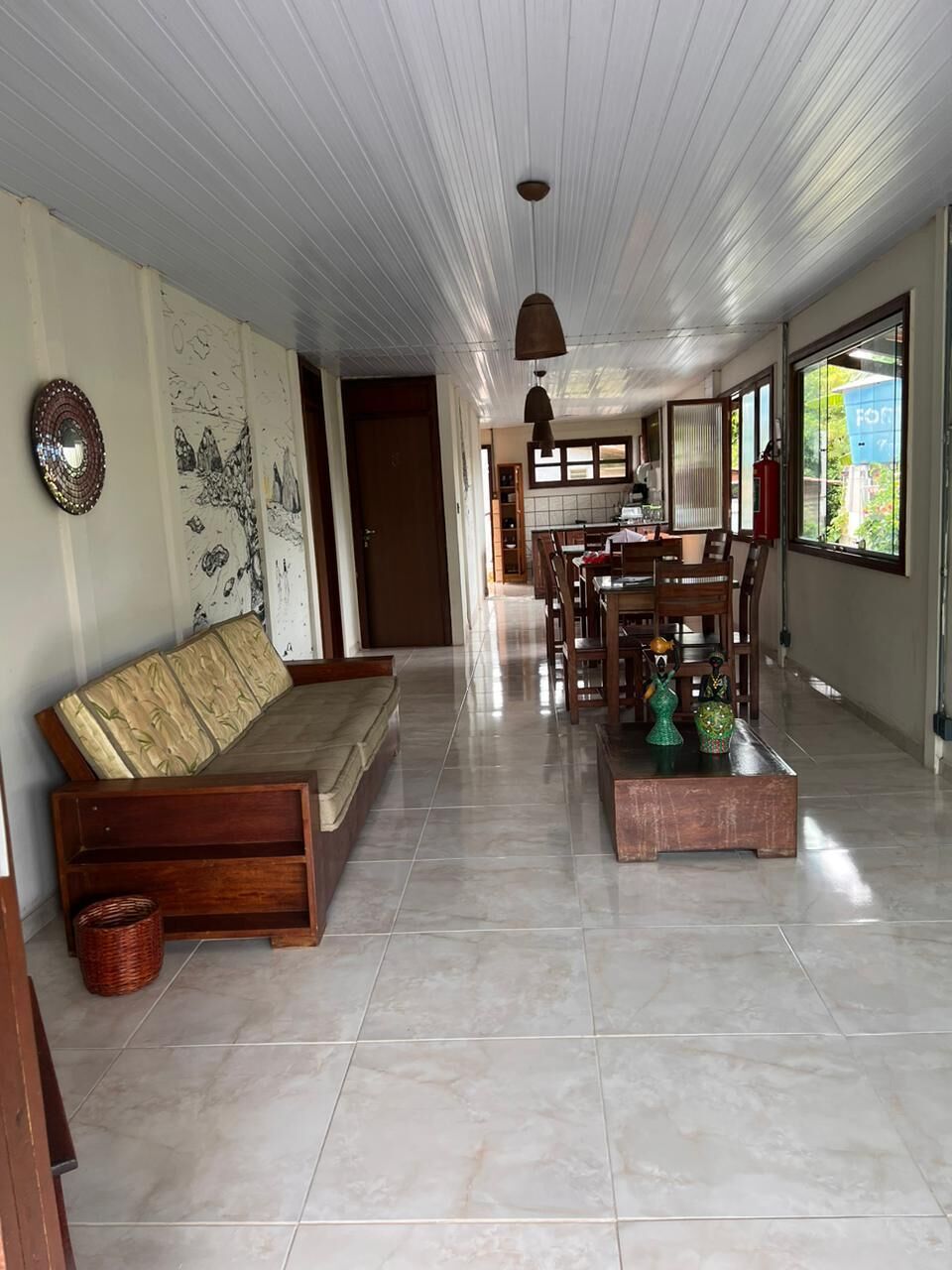 Amplia sala de estar con sofá, mesa de comedor y sillas, piso de baldosas y un plafón con lámpara colgante.