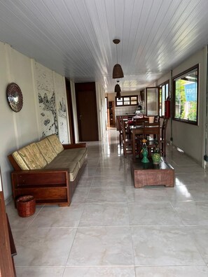 A spacious living area with a sofa, dining table, and chairs, a tiled floor, and a ceiling with a hanging light fixture. - Pousada do Biu (Fernando de Noronha)