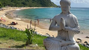Une statue représentant une figure assise, avec une montagne et une plage en arrière-plan.