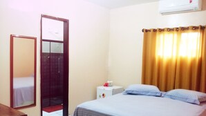 Habitació d'hotel amb un llit, una taula de nit, un mirall i un aparell d'aire condicionat.
