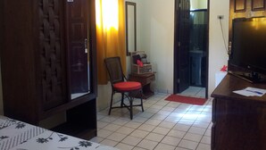 Habitació d'hotel amb un armari de fusta gran, un mirall, una televisió, una taula petita amb una cadira vermella i un sòl de rajola.