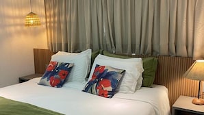 Ein ordentlich bezogenes Bett mit grün-weißer Bettwäsche, zwei Zierkissen, einem Holzkopfende und einer Nachttischlampe.