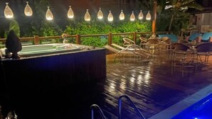 Ein Poolbereich bei Nacht mit Whirlpool und Liegestühlen.