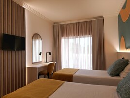 A hotel room with two beds, a desk, a chair, a TV, and a window with curtains.
