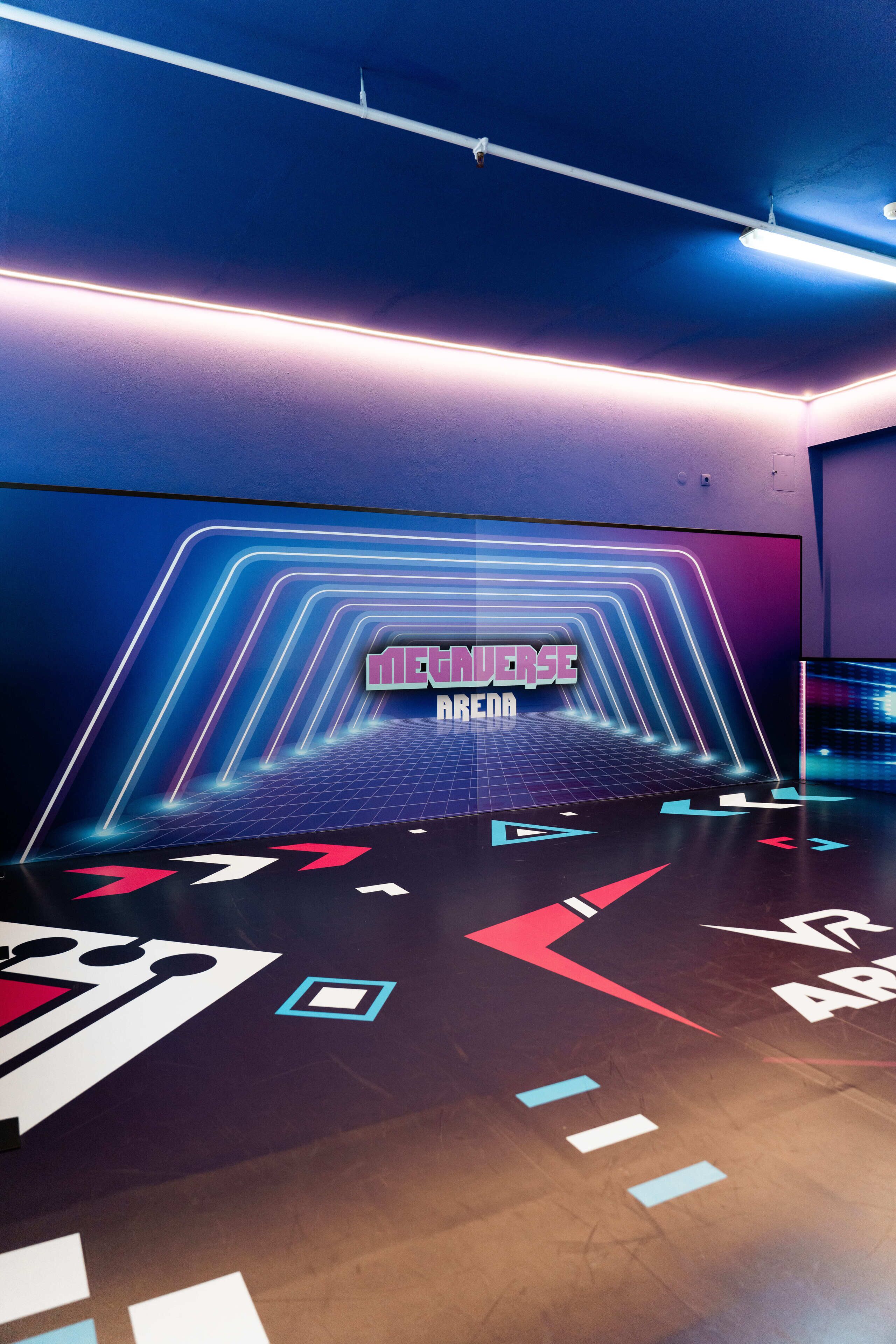 Una habitación futurista con señalización de neón, un diseño geométrico en el suelo y temática de realidad virtual.