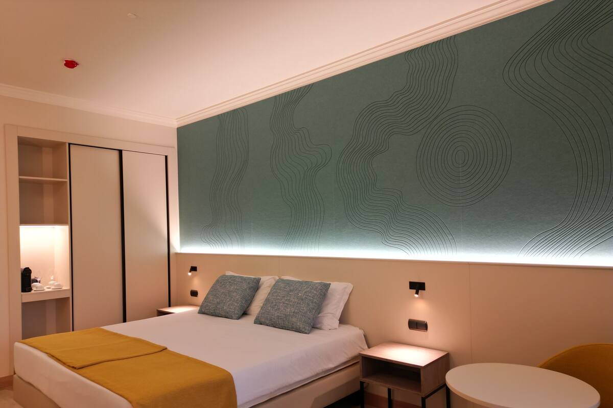 A modern hotel room with a large bed, bedside tables, a small table, and a seating area.